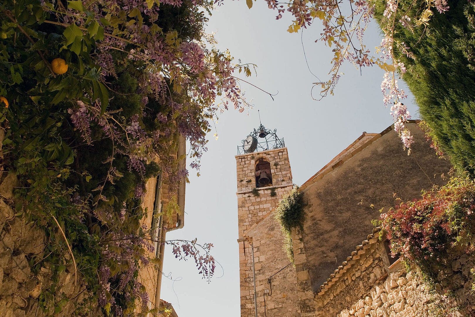 Perched medieval village with stone buildings clustered on hillside, olive groves in foreground, panoramic valley views of Provence