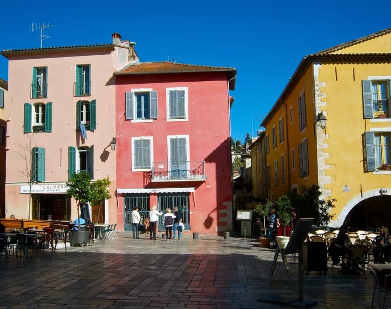 Maisons roses et ocre aux volets verts sur une place du village de Valbonne