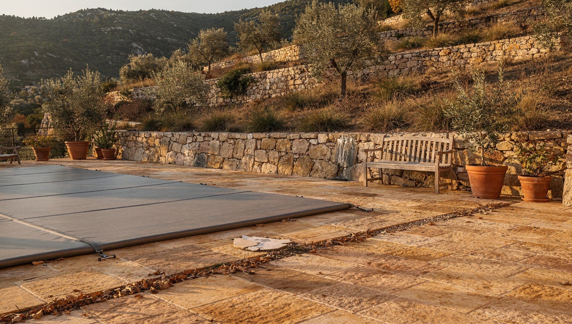 Stone pool terrace above olive restanques near Opio in the Riviera hinterland, the pool covered for winter in late-afternoon autumn light