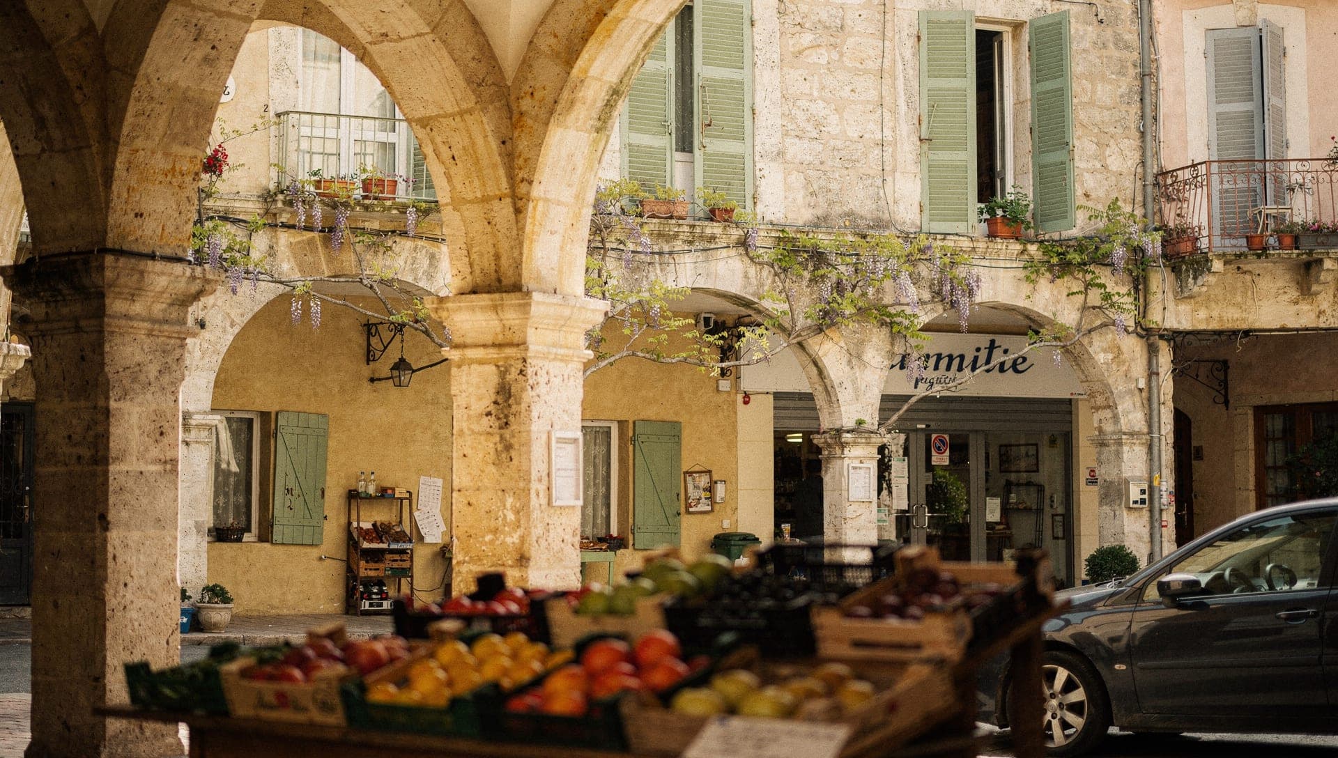 Ruelle en pierre ensoleillée du centre historique de Grasse avec façades provençales à volets s'élevant sur la colline au-dessus de la ville du parfum