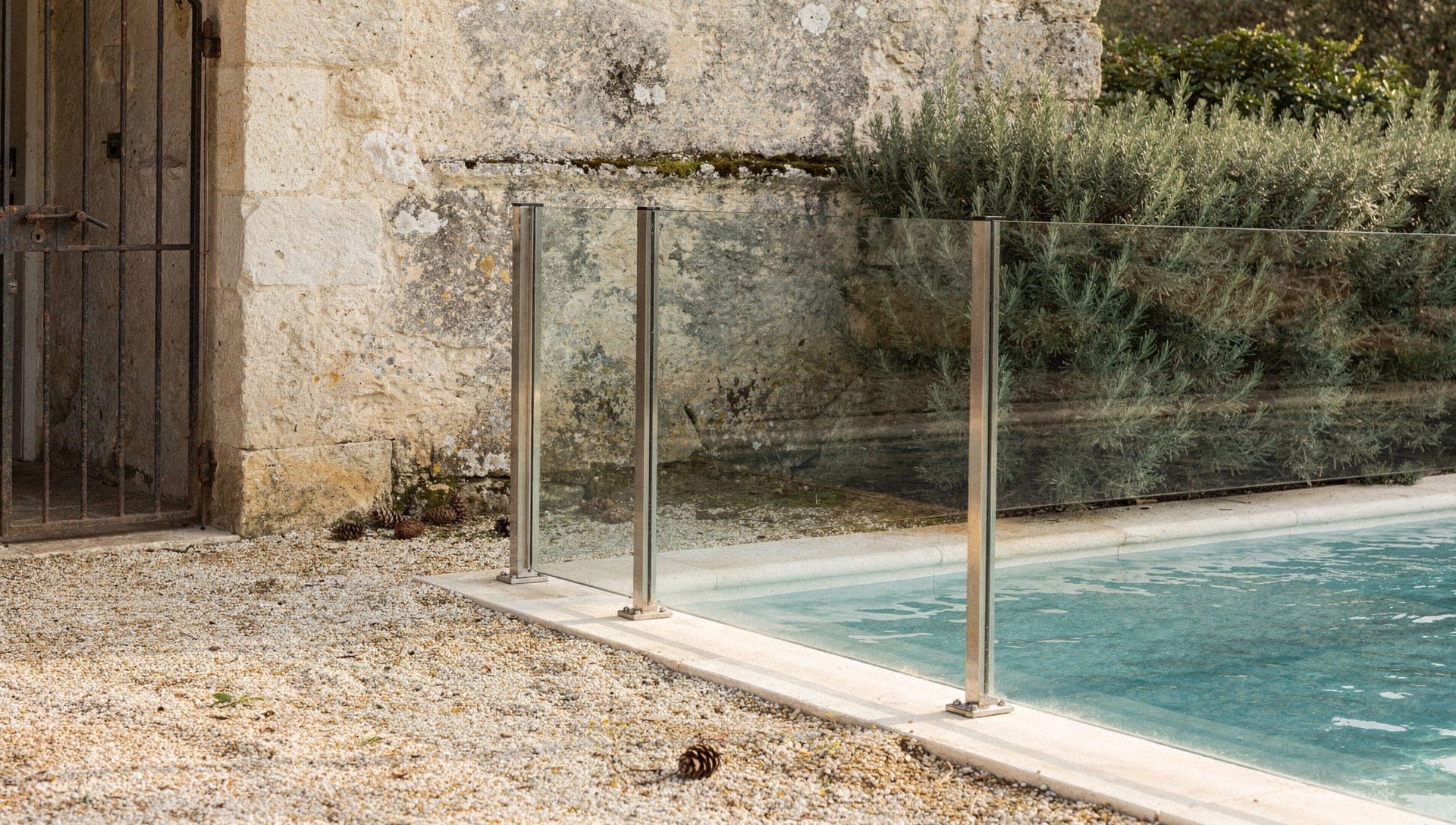 Glass pool safety fence beside a weathered limestone wall and rosemary hedge on a Riviera hinterland villa terrace